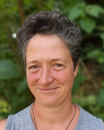 Porträt von Jana Elke vor grünem Laub.