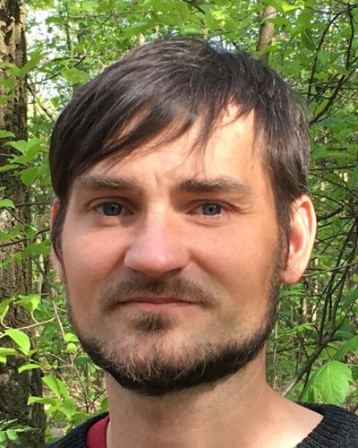 Porträt von René Landmann vor grünem Laub.